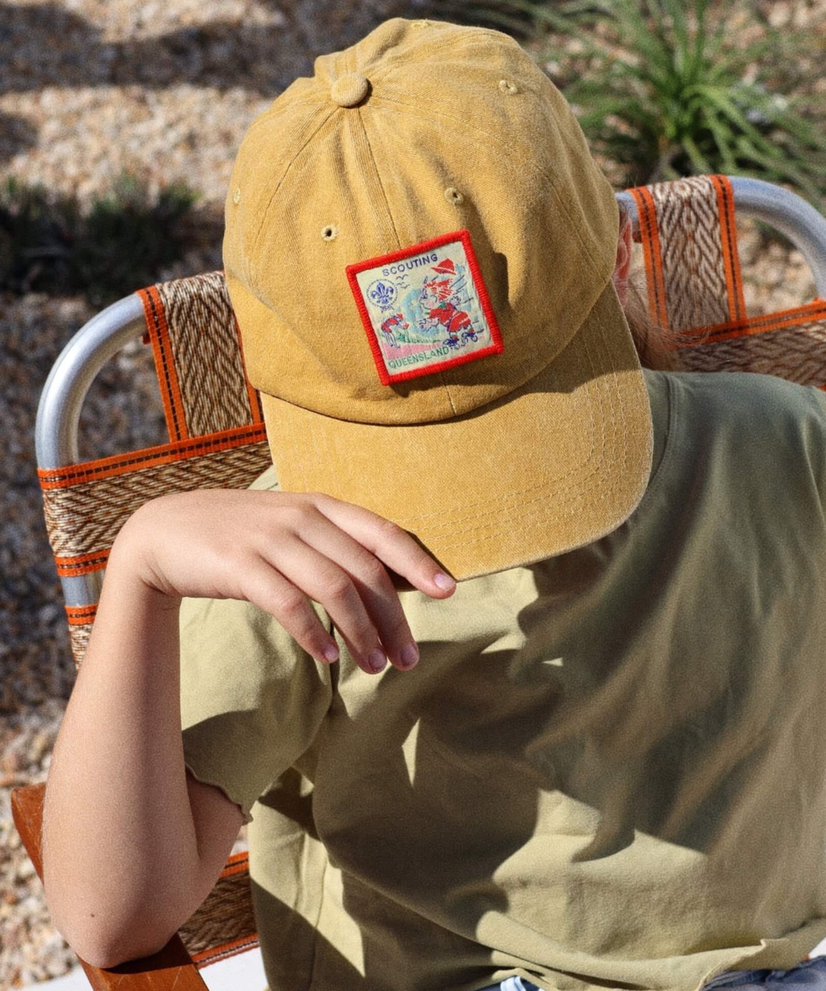 child wearing a mustard cap with a colorful patch, sitting outdoors.
