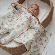 Baby in a wicker bassinet wearing Kailani zip suit, wrapped in matching coastal-print swaddle in cream and soft blue.