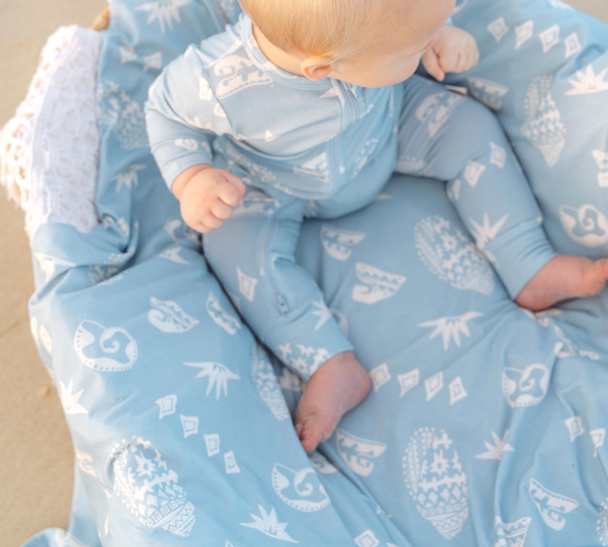 Baby lying on a soft blue Kailani shell print swaddle by Bam Loves Boo