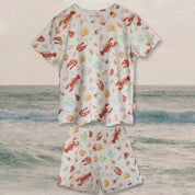 kids Pajamas in cream with Aussie summer print (lobsters, prawns, shells, sun, thongs); long sleeves; beach backdrop.