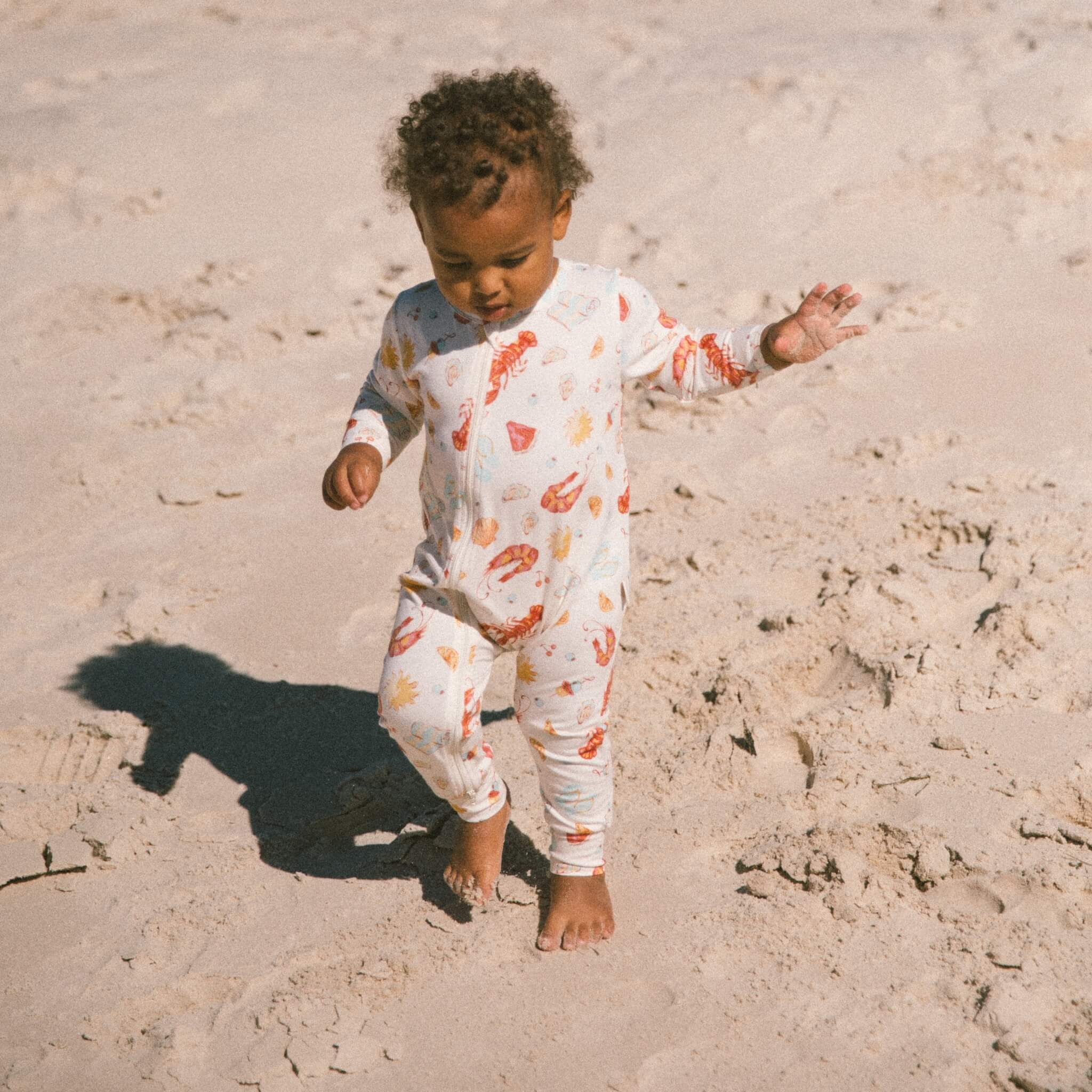 Baby wearing cream Australian-summer printed bamboo jumpsuit on the sand