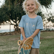 Child holding a skateboard outdoors with trees and grass in the background