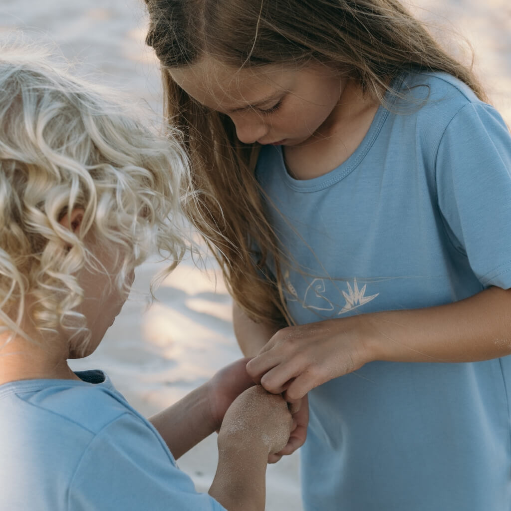 Two children in blue shirts holding hands on a beach.