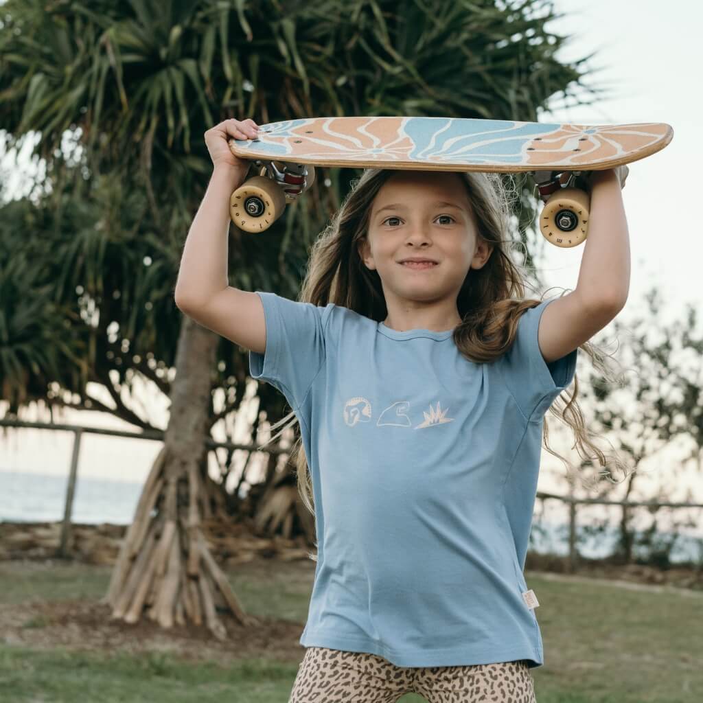 Child in Blue Bamboo Tee holding a skateboard on their head