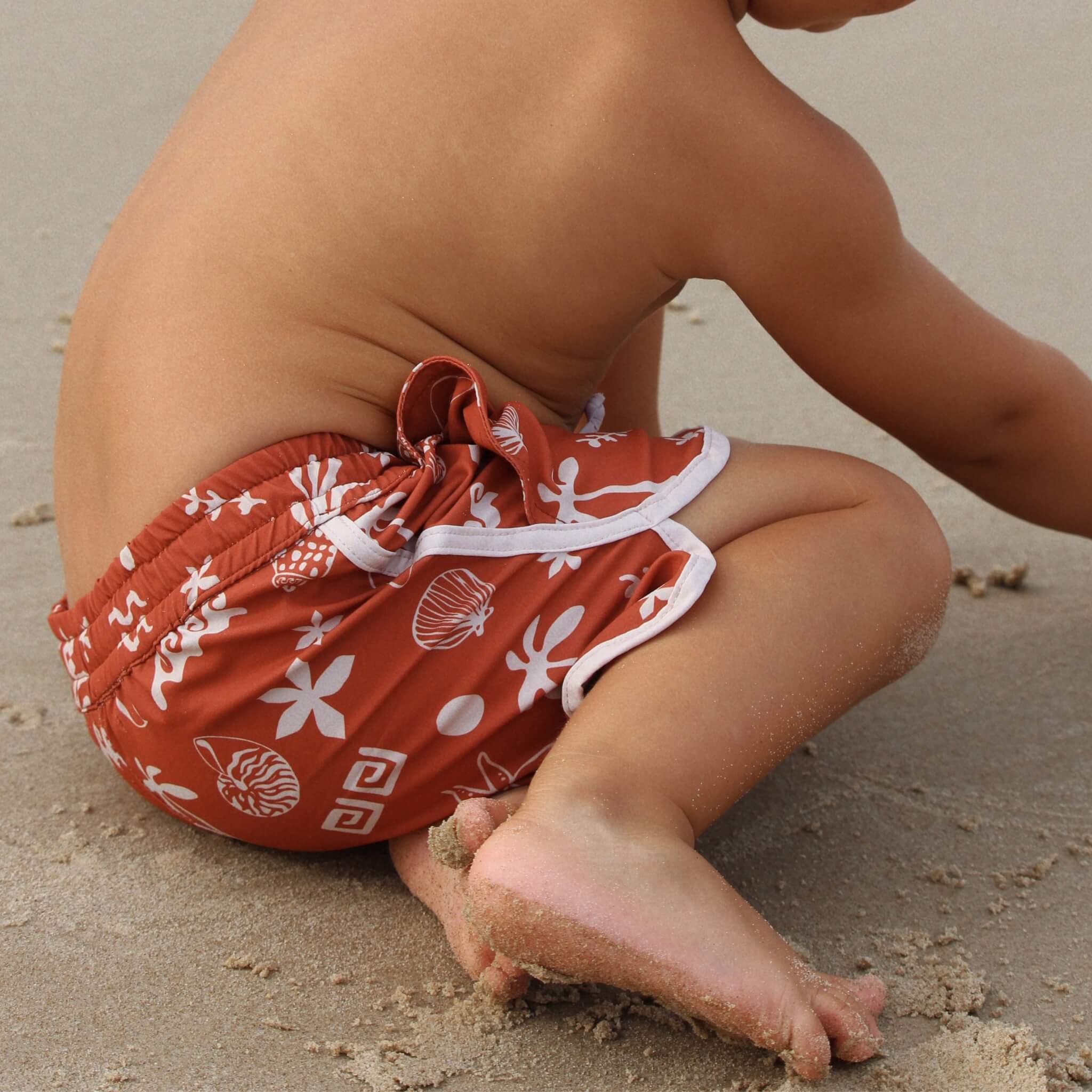 Boy  on sand wearing red boardies on beach