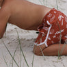 Boy crawling on Australian beach wearing red boardshorts