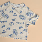 Flat lay of Kailani tee with full view of the coastal shell and wave pattern in soft blue on cream cotton.