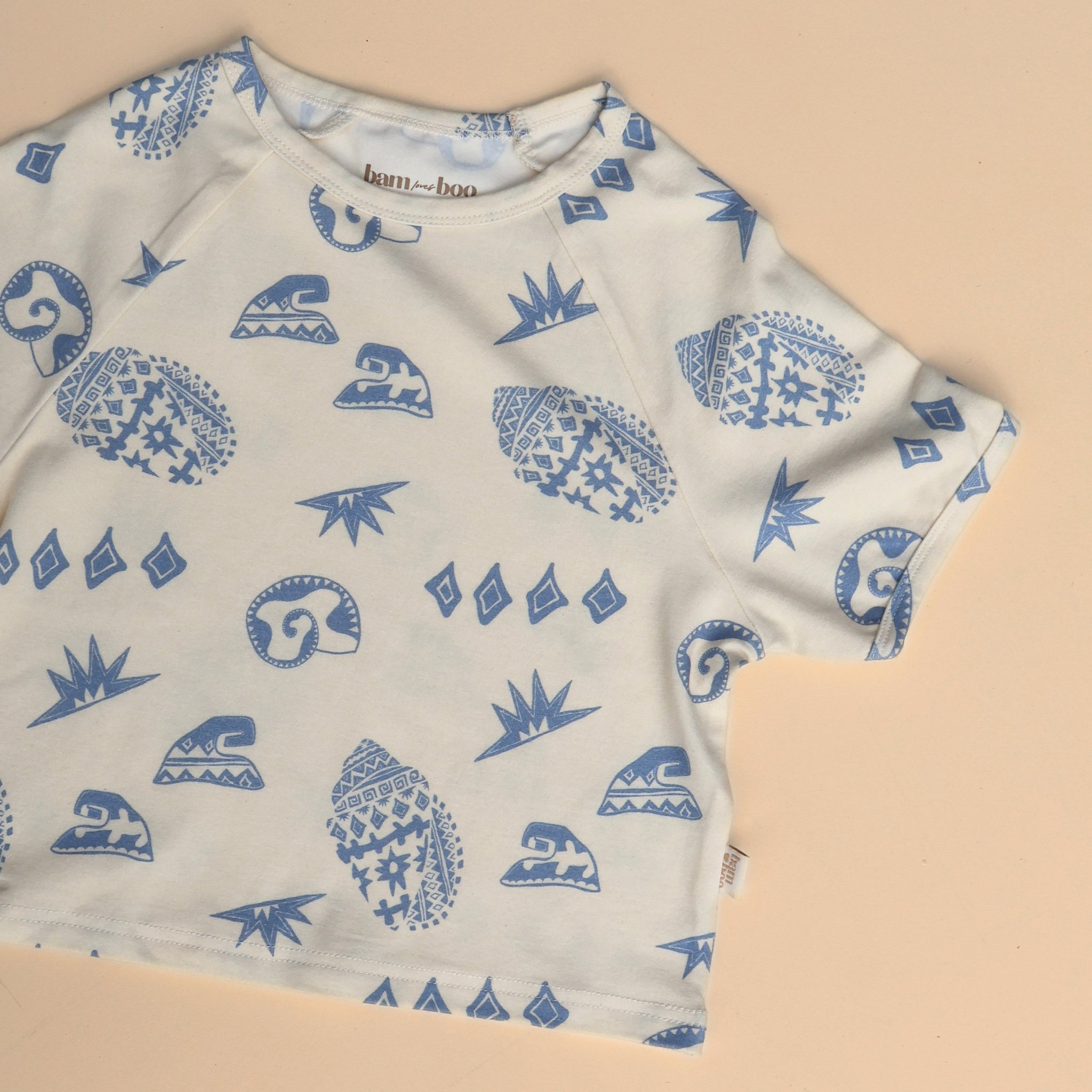 Flat lay of Kailani tee with full view of the coastal shell and wave pattern in soft blue on cream cotton.