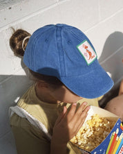 Person wearing a blue cap with a logo, eating popcorn from a box.