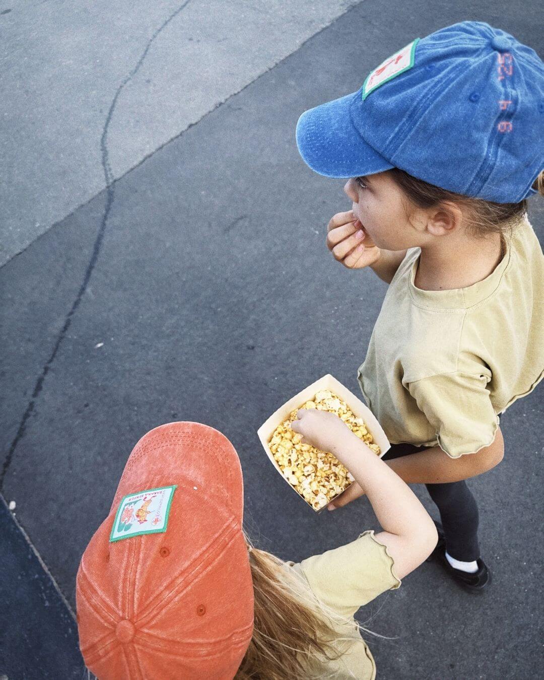 Child in a blue cap eating popcorn on concrete