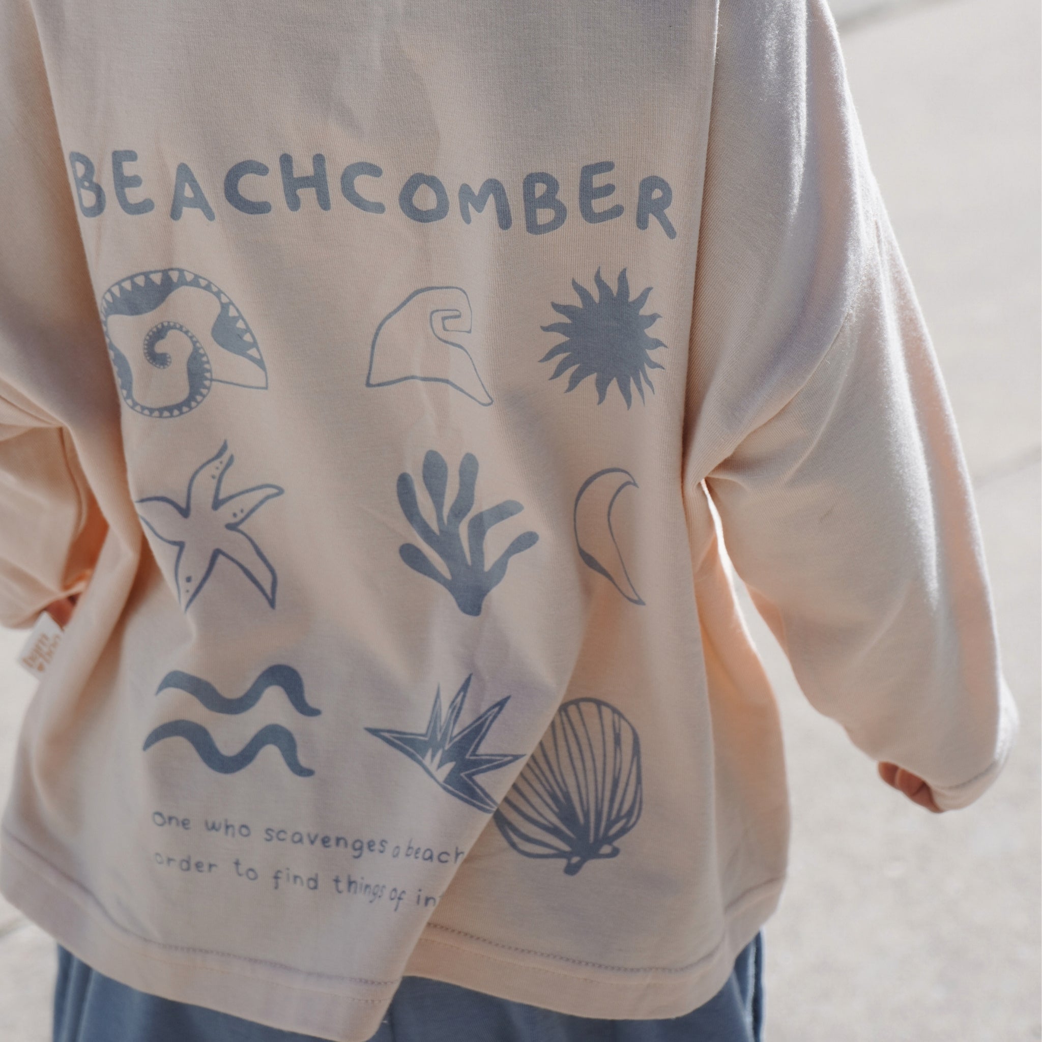 Back view of child wearing the Beachcomber long sleeve tee in bamboo organic cotton, featuring ocean-inspired illustrations in soft blue.