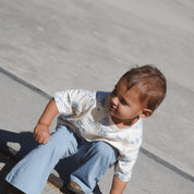 Child in Kailani tee and blue pants outdoors, at skatepark photoshoot.

