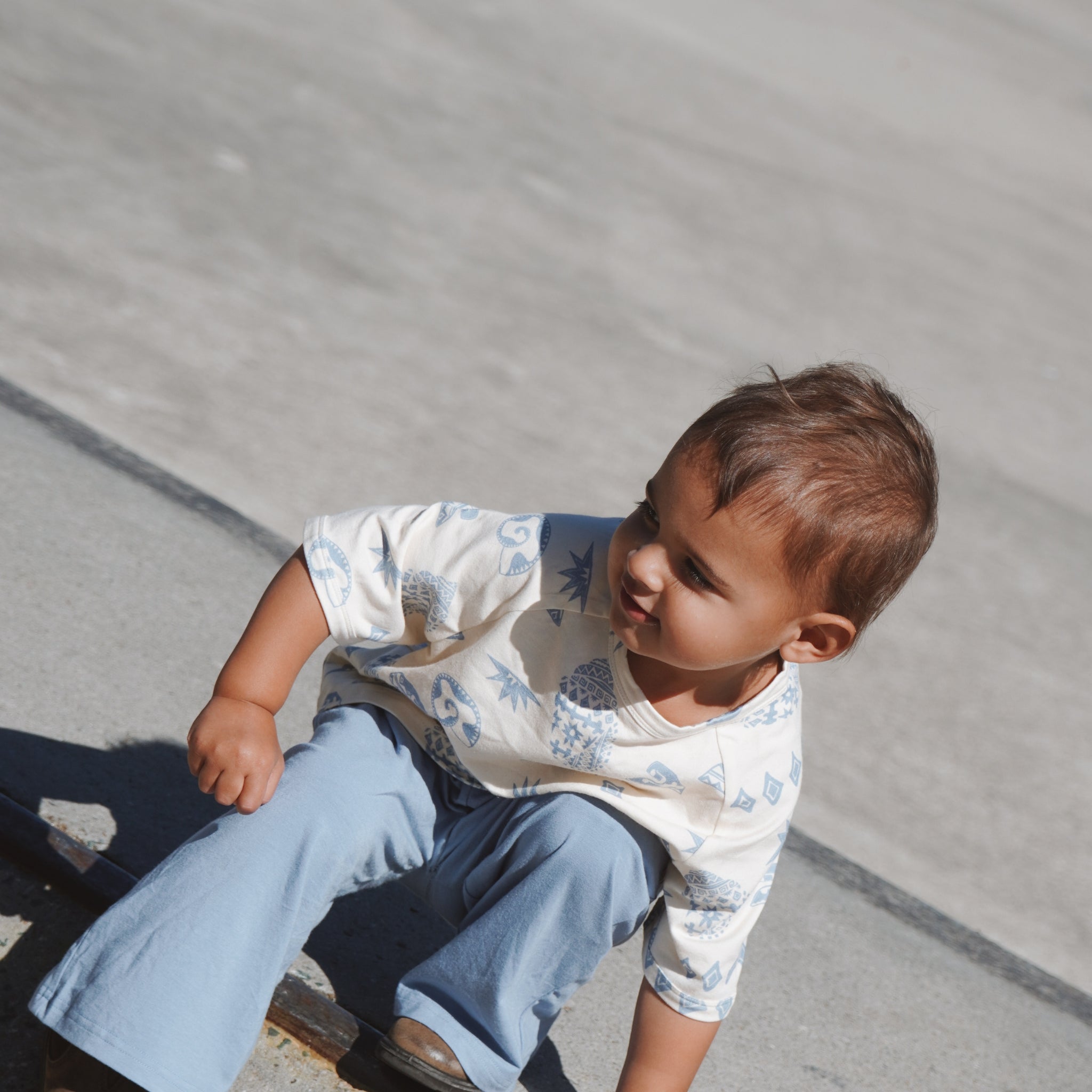 Child in Kailani tee and blue pants outdoors, at skatepark photoshoot.

