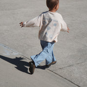 Child running on a sidewalk wearing a light-colored sweatshirt with graphics and blue pants.