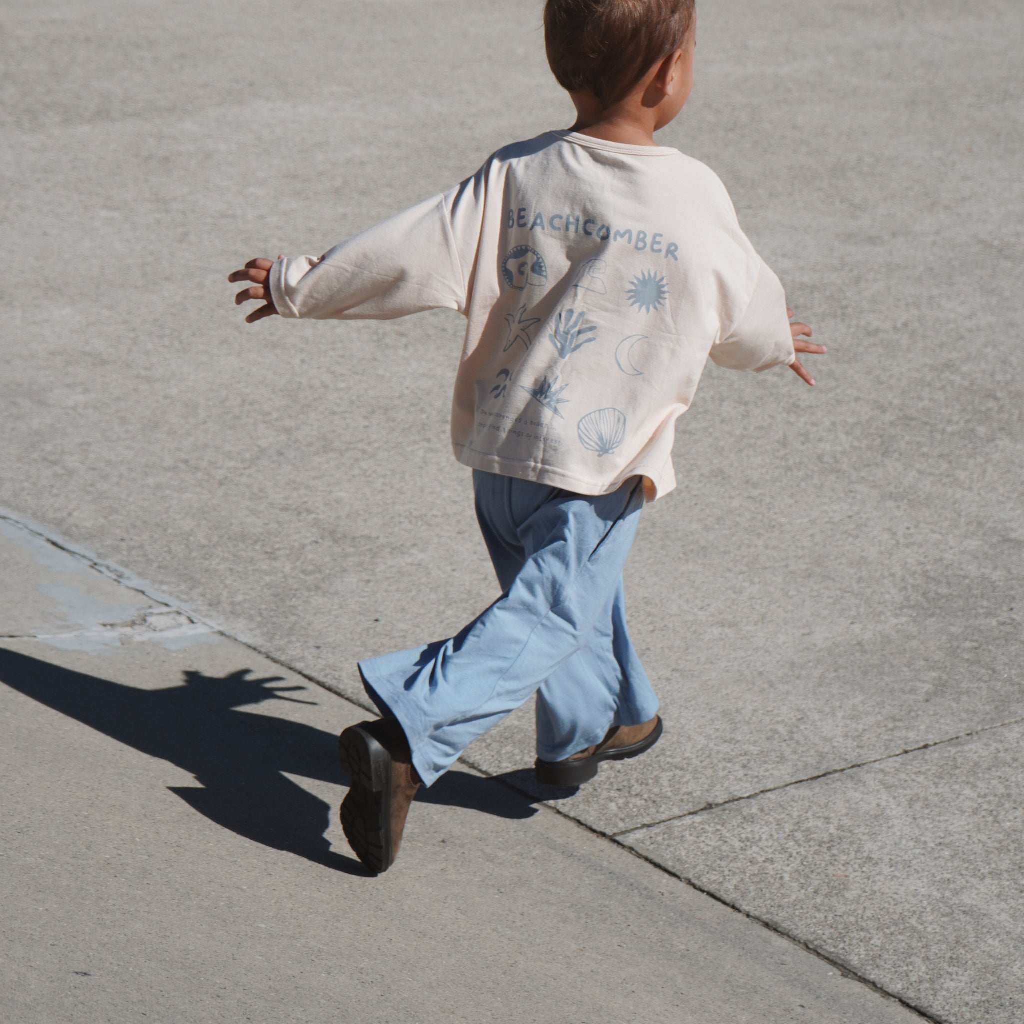 Child running on a sidewalk wearing a light-colored sweatshirt with graphics and blue pants.