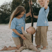 Three children playing on a sandy beach wearing matching blue shirts and leopard print pants.
