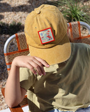 child wearing a mustard cap with a colorful patch, sitting outdoors.