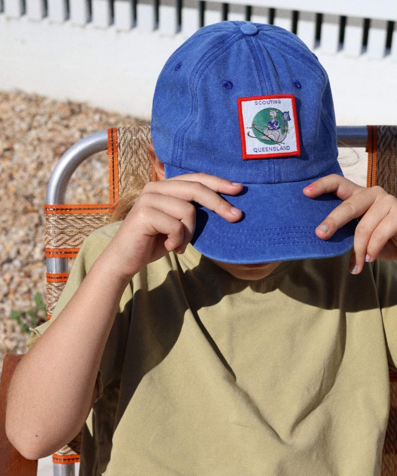 child wearing a blue cap with a Queensland patch, sitting outdoors.