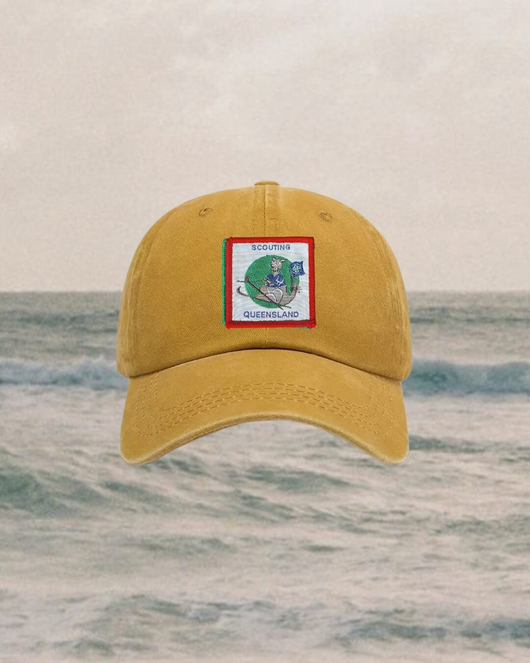 mustard Yellow dad cap with a logo on a ocean background