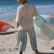 child wearing cream tee and blue and cream stripe pants on the beach with inflatable