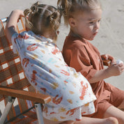 kids wearing Aussie summer print PJ's lobsters, prawns, shells, sun sitting on a chair