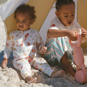 baby and child wearing cream Australian-summer print onesie and tee sitting on the beach playing.