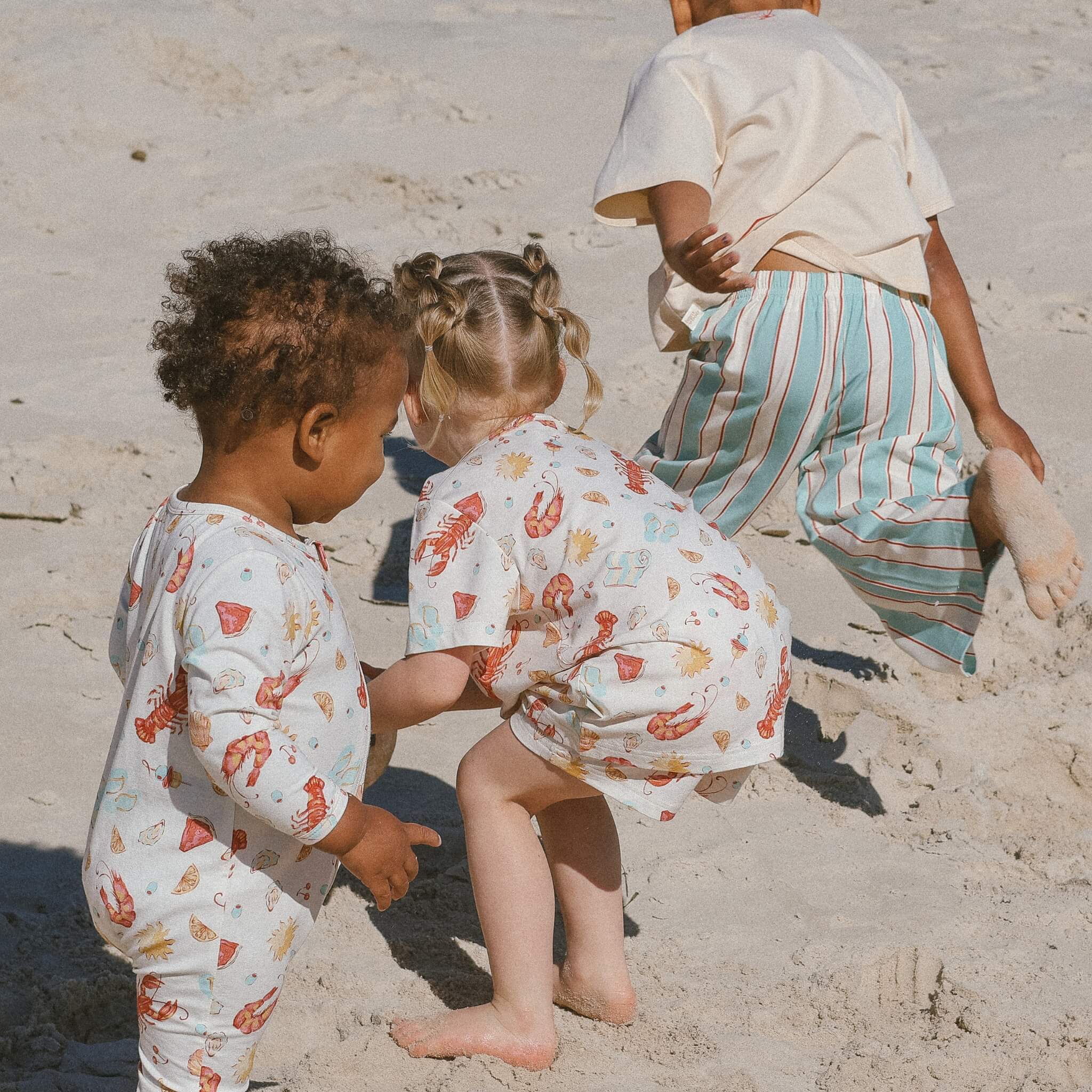 children playing in the sand wearing an Aussie christmas collection PJs and jumpsuits