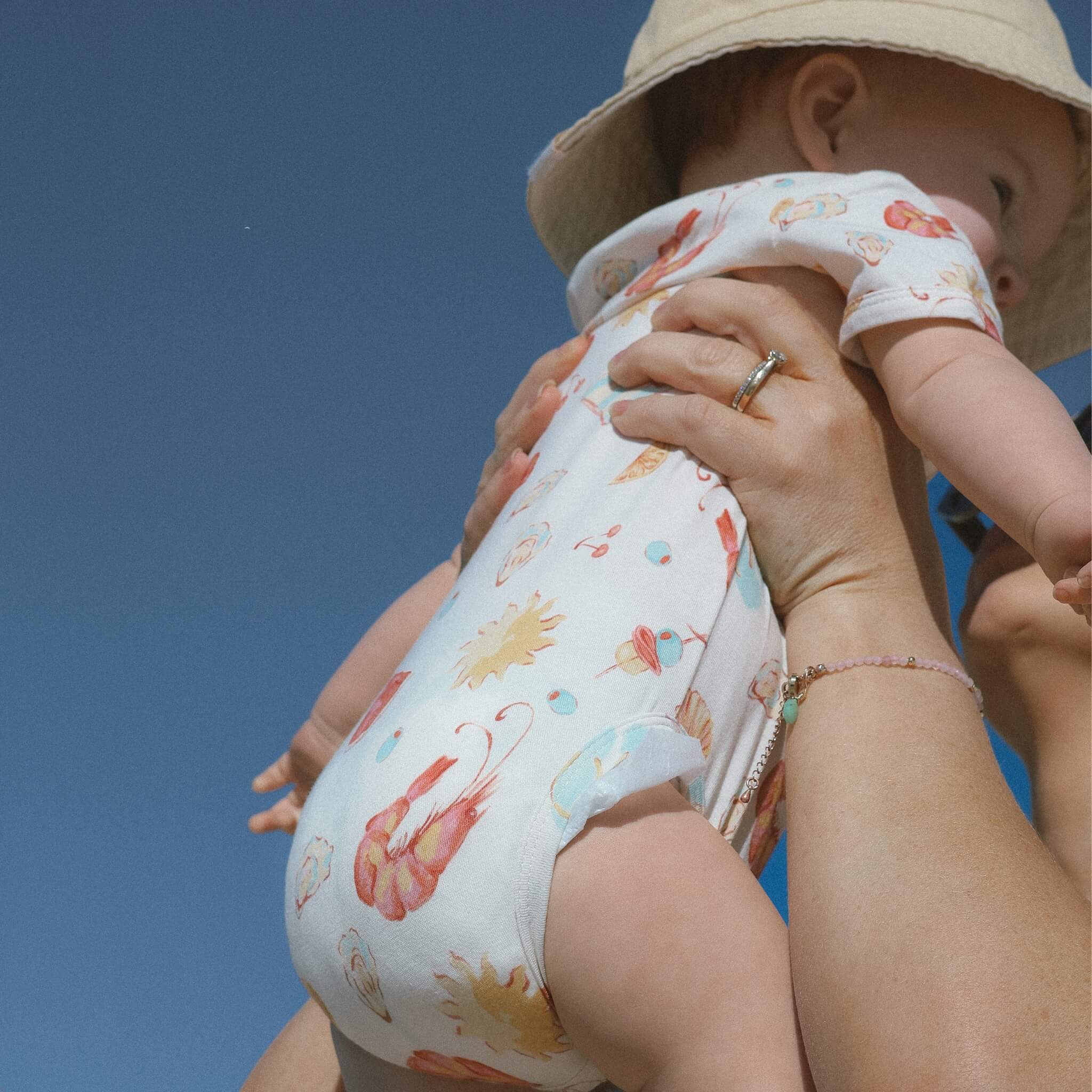 Baby wearing cream printed onesie with suns shrimps lobsters for christmas
