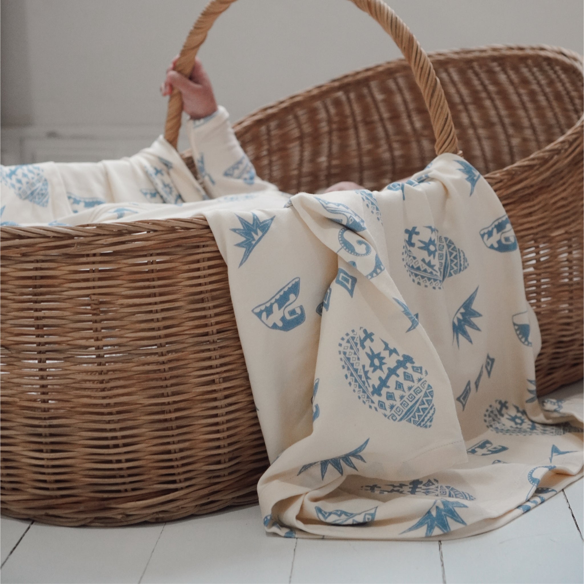 Kailani swaddle being lifted from a wicker basket, showcasing its large size and coastal print.