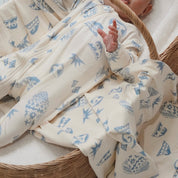 Close-up of baby in Kailani print zip suit, surrounded by matching swaddle with shells, waves, and sun motifs.