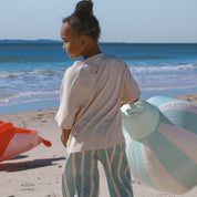 kid in boxy cream tee featuring shell, and wave print paired with mint pinstripe pants on the beach.