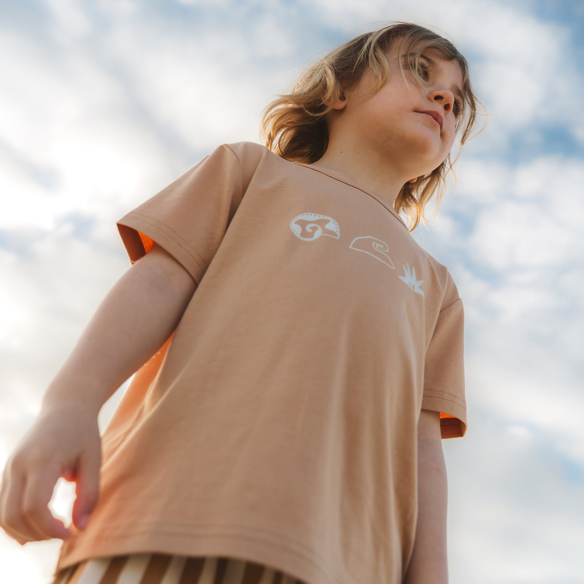 Close up of a child in a tan Beachcomber print tee against the sky by Bam Loves Boo