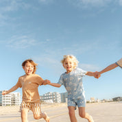 Kids running hand in hand along the beach in Kailani print pyjama sets by Bam Loves Boo