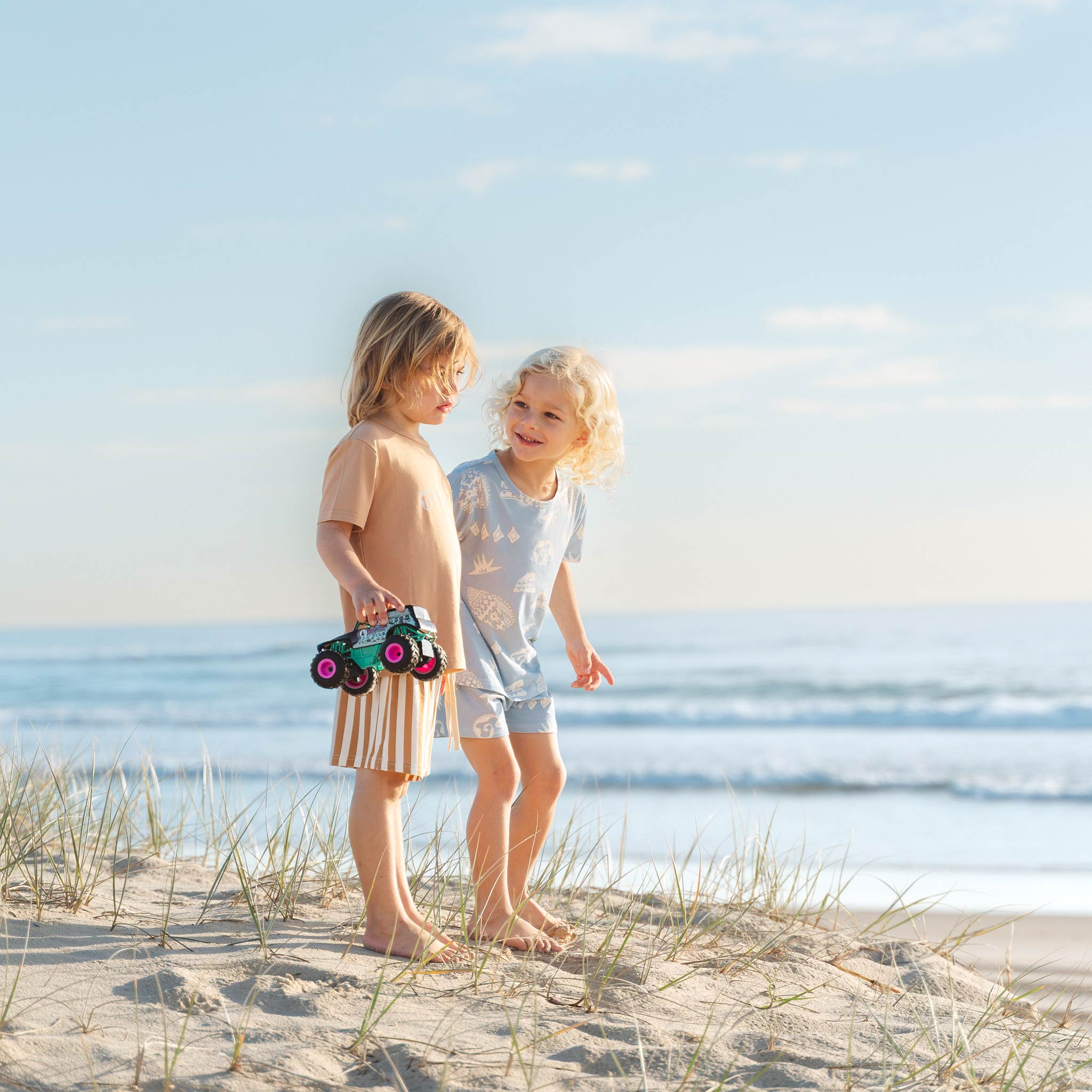 Kids chatting on the beach in tan and blue Kailani print pyjama sets by Bam Loves Boo