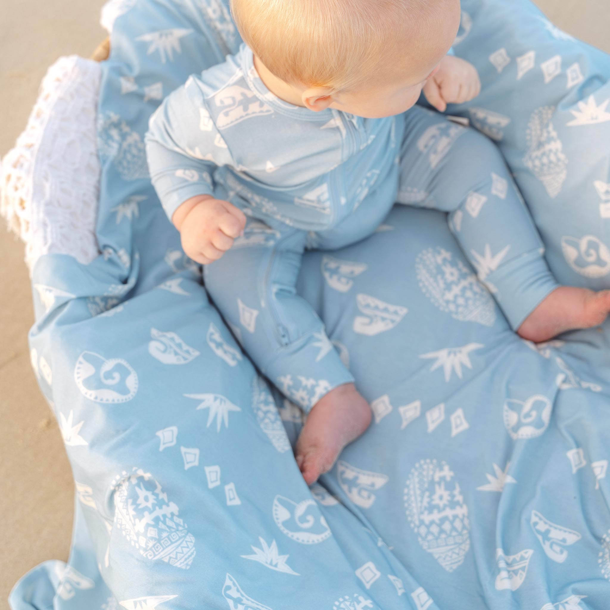 Baby lying on a blue Kailani shell print swaddle by Bam Loves Boo