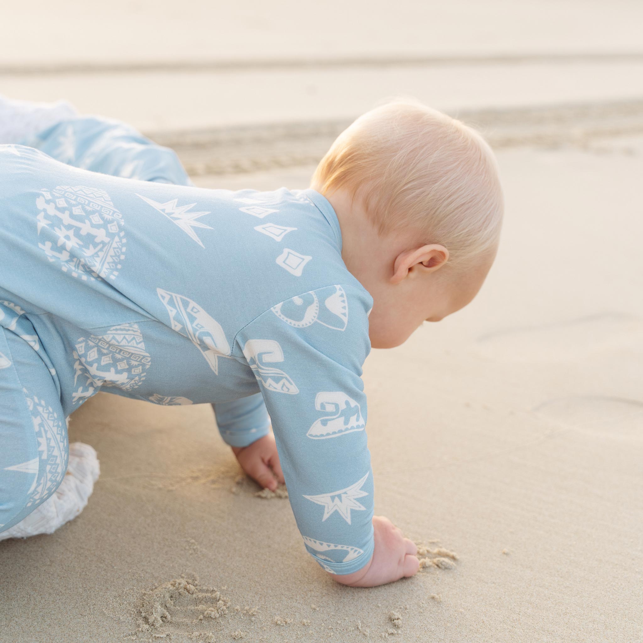 Close up of a baby crawling in the blue Kailani shell print zip jumpsuit by Bam Loves Boo