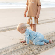 Baby crawling on the sand in a blue Kailani shell print zip jumpsuit by Bam Loves Boo