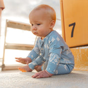 Baby sitting in the sand in a blue Kailani shell print zip jumpsuit by Bam Loves Boo
