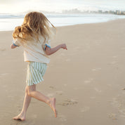 Child running along the beach in a cream Kailani shell print raglan tee by Bam Loves Boo