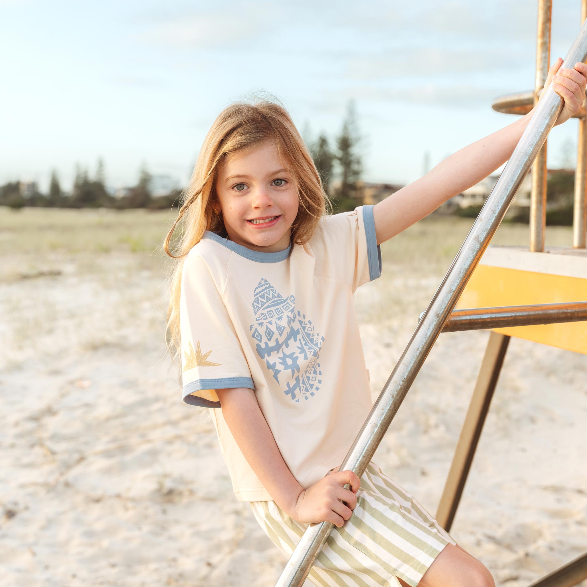 Child smiling in a cream Kailani shell print raglan tee by Bam Loves Boo