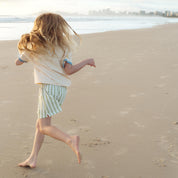 Child running on the sand in sage green and cream striped shorts by Bam Loves Boo