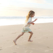 Child running along the beach in sage green and cream striped shorts by Bam Loves Boo