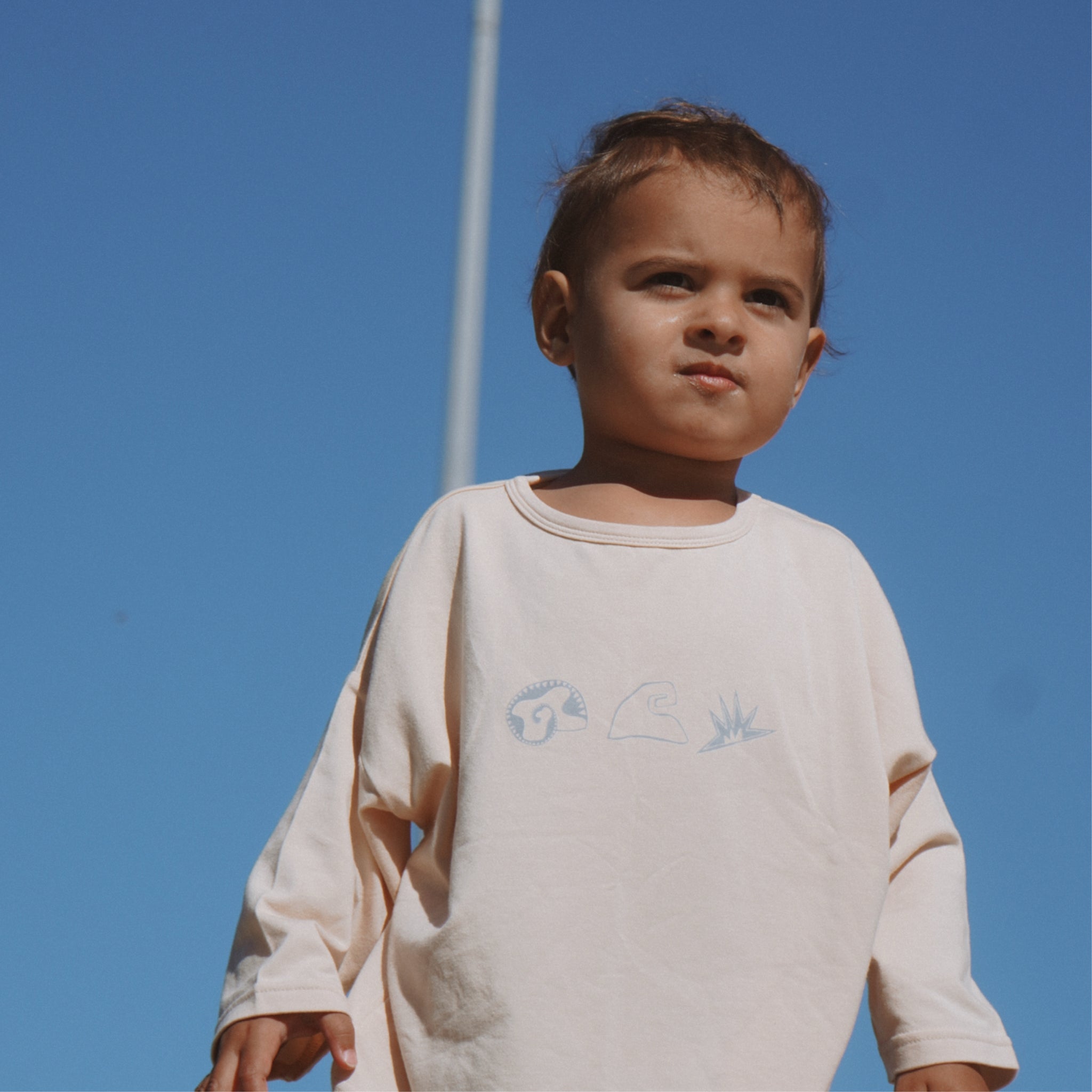 Child wearing a light-colored long-sleeve shirt against a clear blue sky