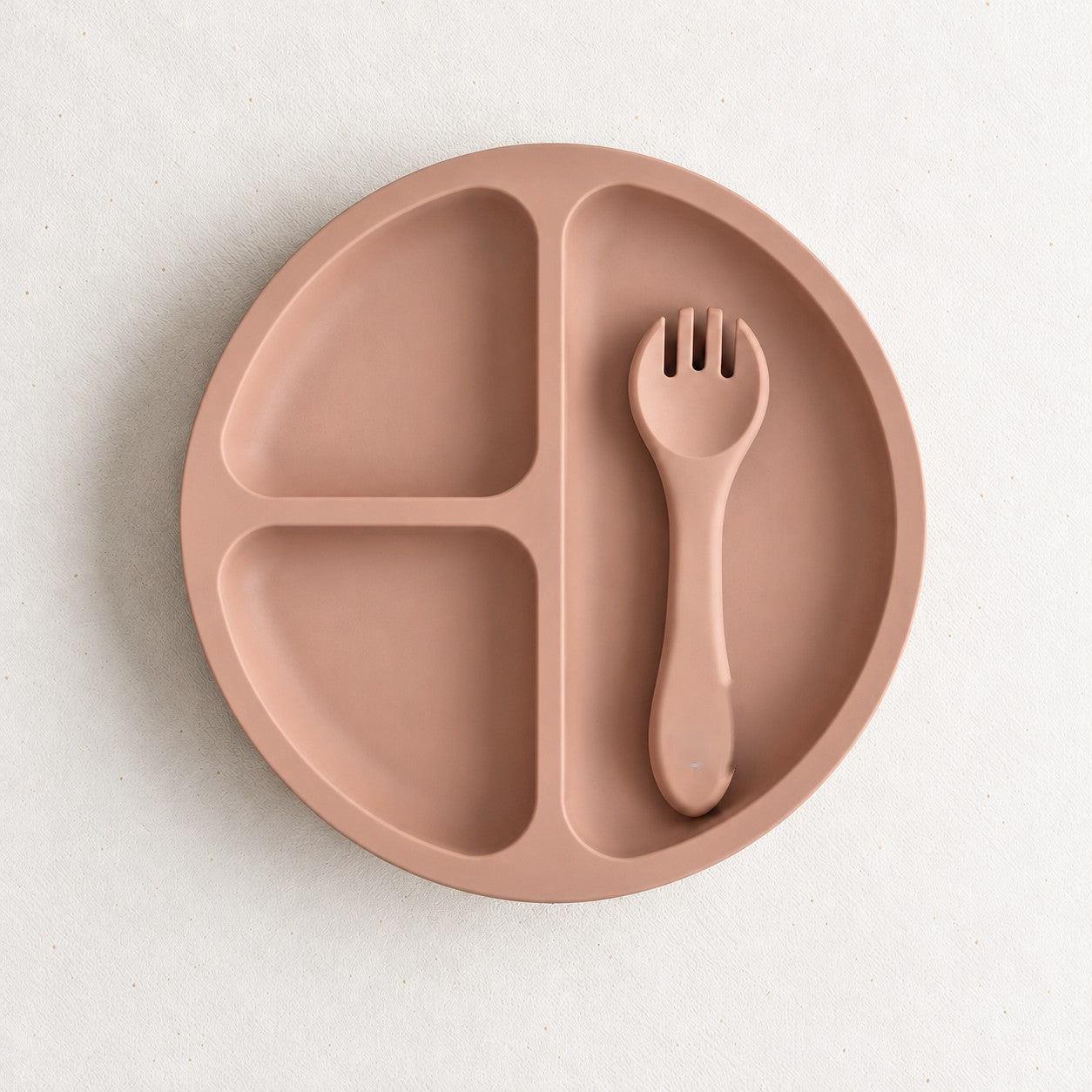 Peach silicone bento plate with three sections and matching fork, on a soft stone background