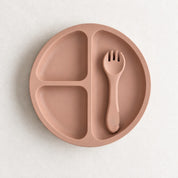 Peach silicone bento plate with three sections and matching fork, on a soft stone background