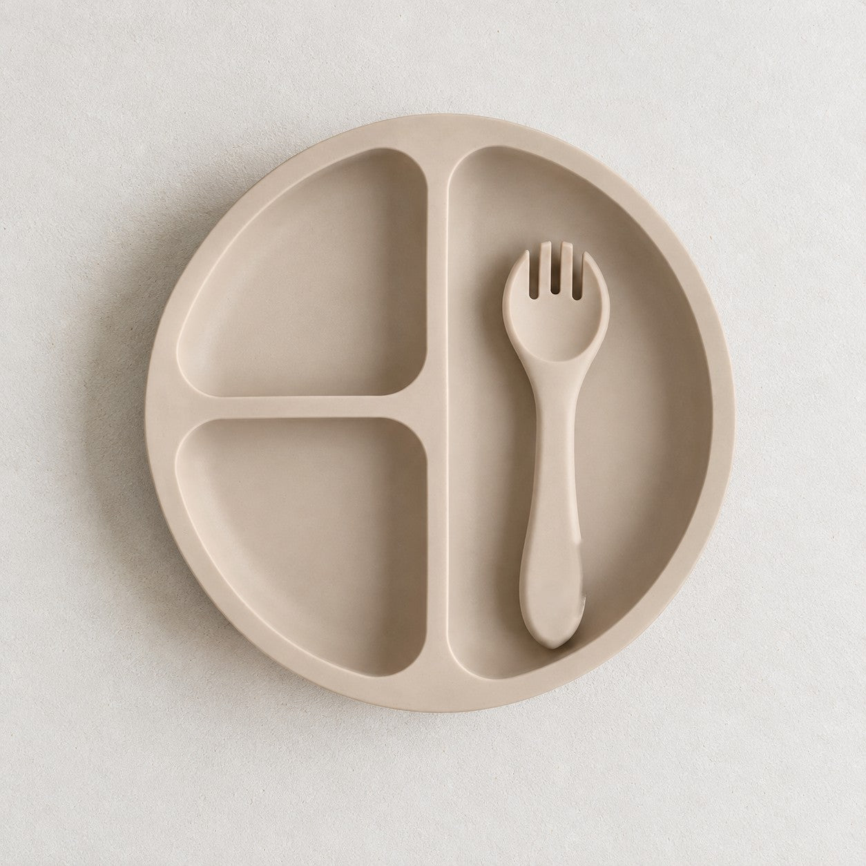 Sand silicone bento plate with three sections and matching fork, on a soft stone background