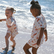 kids playing in waves wearing cream with Aussie christmas print lobsters, prawns, shells, sun.