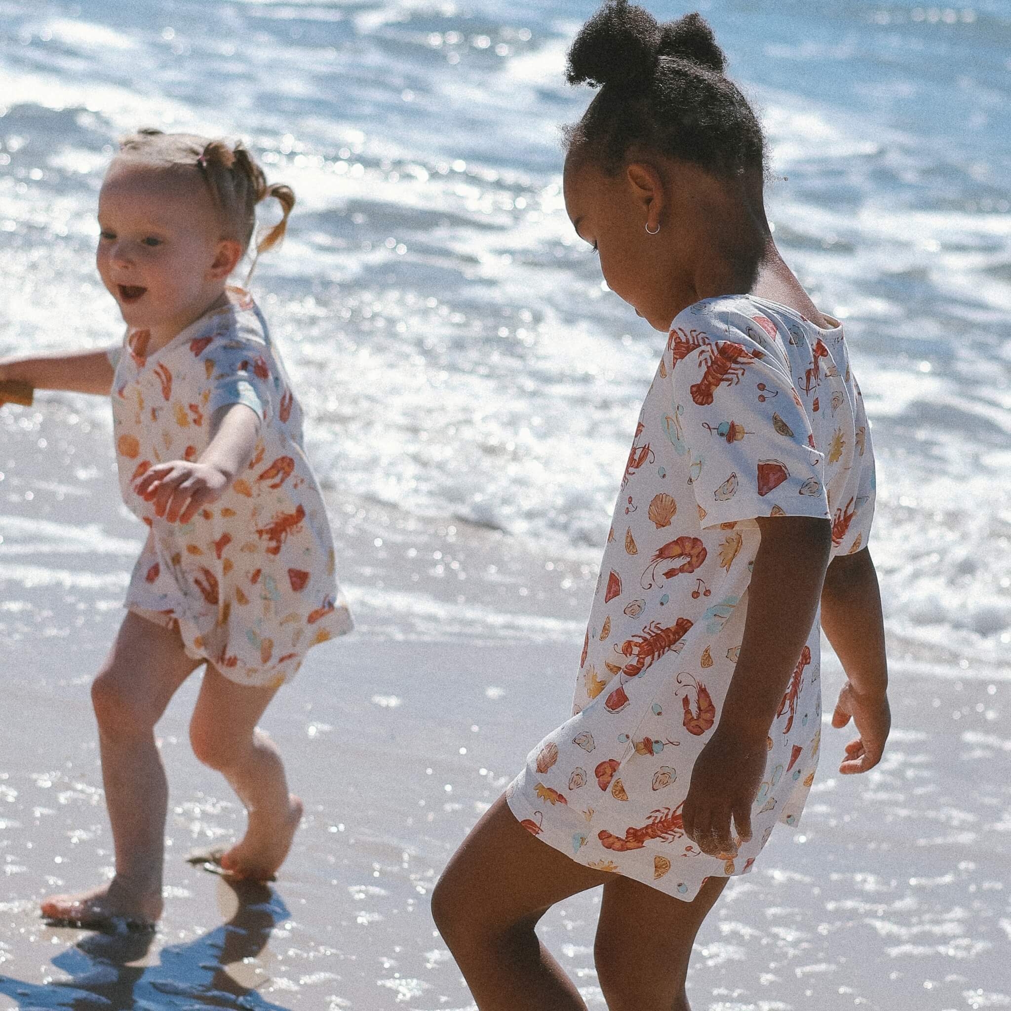 kids playing in waves wearing cream with Aussie christmas print lobsters, prawns, shells, sun.