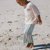 child wearing cream tee and blue and cream stripe pants running on the beach