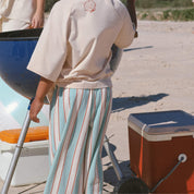 child wearing cream tee and blue and cream stripe pants on the sand